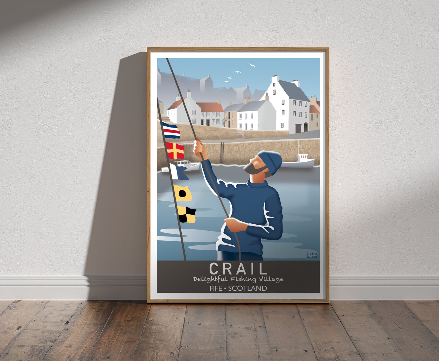 Framed illustration of a sailor raising nautical flags at Crail harbour, with historic white houses with crow stepped gables in the background 