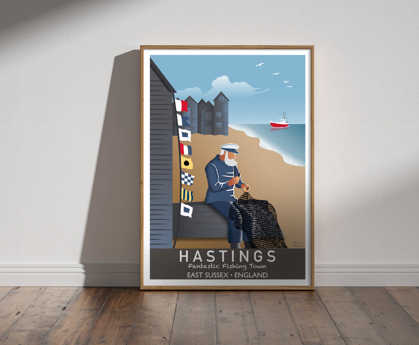 Framed illustration of a fisherman mending his nets at Hastings seafront, with nautical flags and old fishing shacks in background 