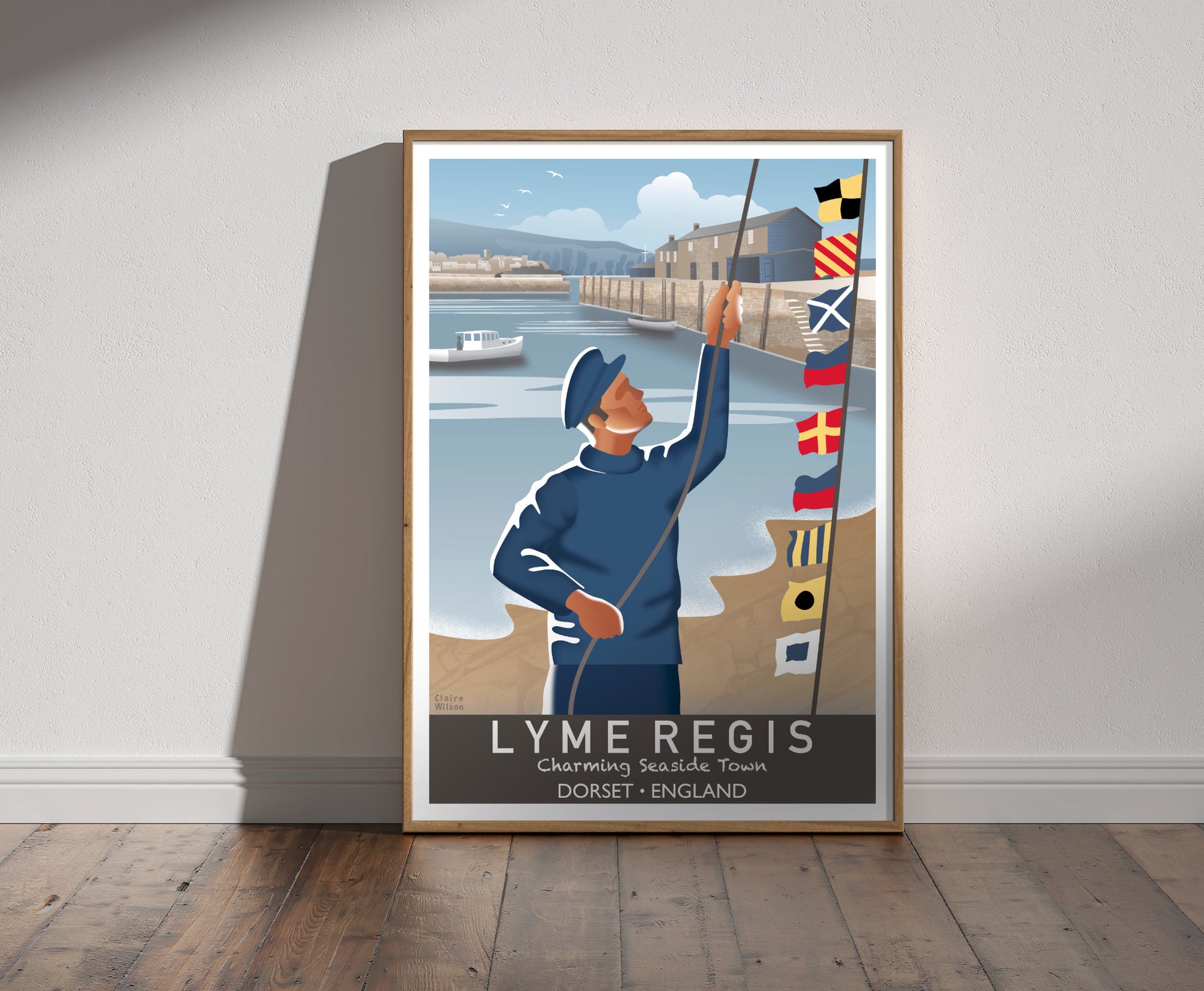 Framed illustration of a sailor raising nautical flags at Lyme Regis harbour, with a seaside town and fishing shacks in background 