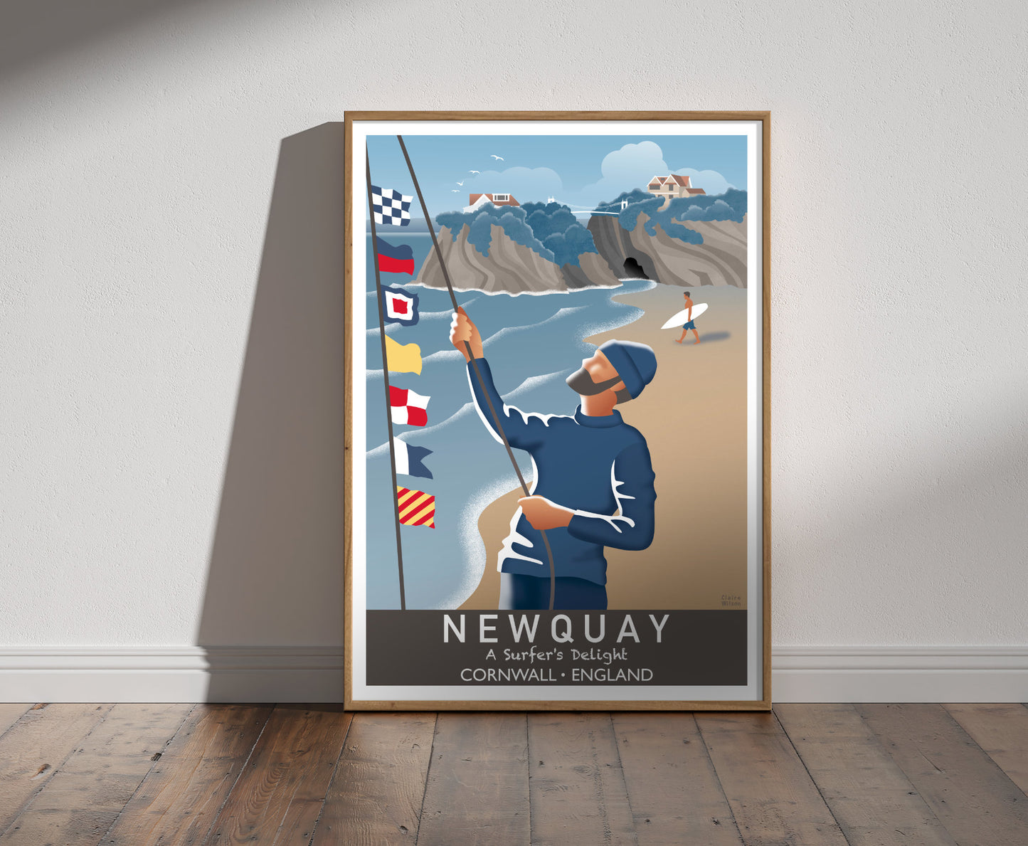 Framed illustration of a sailor raising nautical flags on Newquay beach, with a house on a craggy island and a surfer in background 