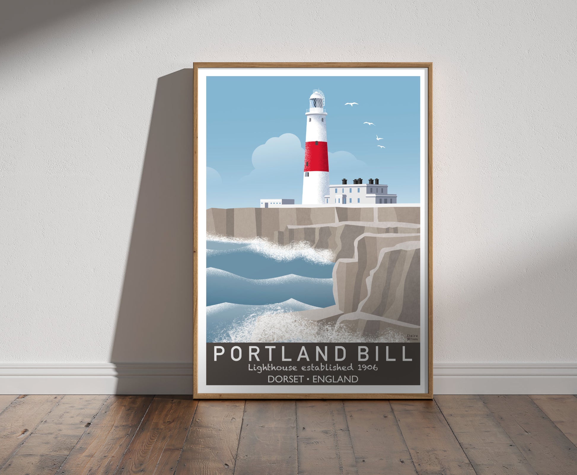 Framed illustration of a white and red striped lighthouse, white buildings, and a rough sea crashing against rugged rocks