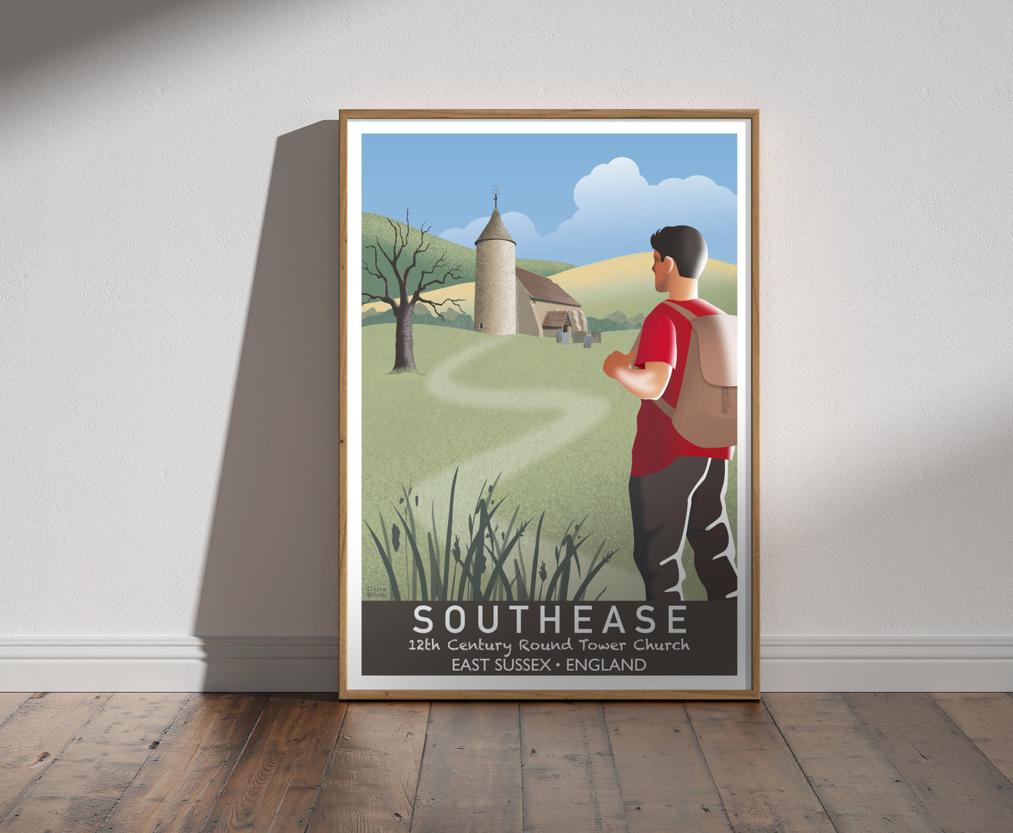 Framed illustration of a man hiking, looking at a church with a round tower, a gnarled tree and countryside hills in the background