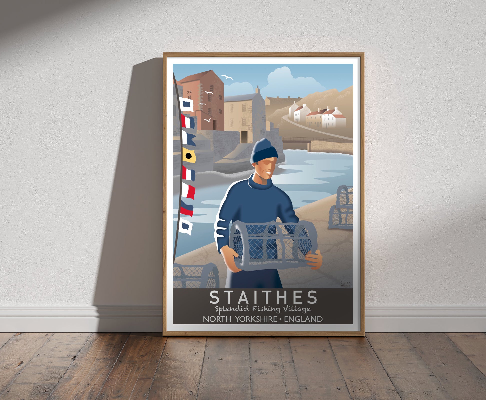 Framed illustration of a sailor carrying lobster trap, with nautical flags at Staithes harbour, and historic houses in the background 