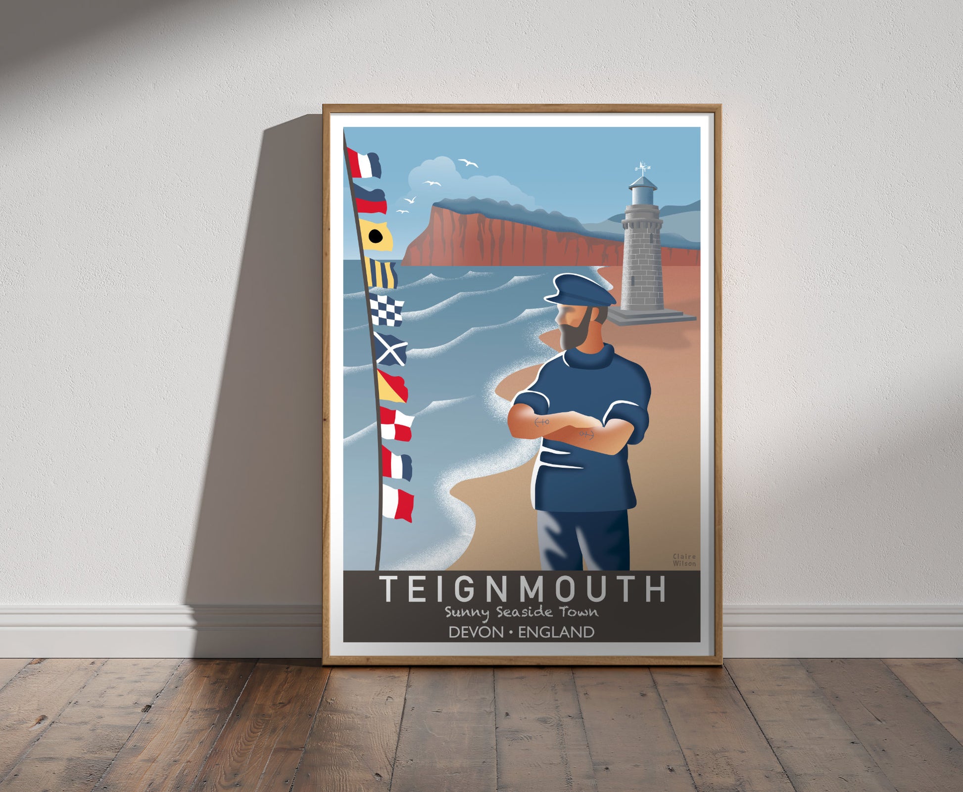 Framed illustration of a sailor and nautical flags at Teignmouth seafront, with a lighthouse and red cliffs in background 