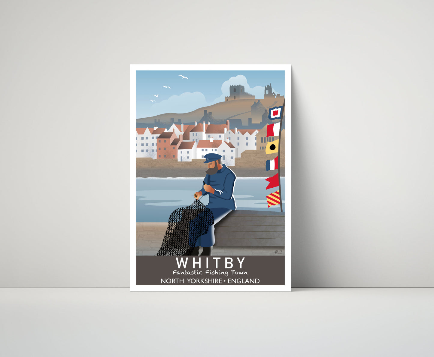 Artwork of a seafarer fixing his fishing nets at Whitby, with maritime flags, seaside village in the distance, and a church and abbey on a hill