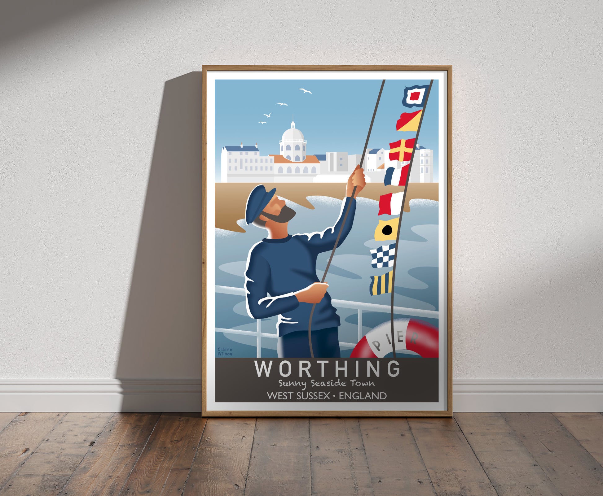 Framed illustration of a sailor raising nautical flags on Worthing pier, with a seaside town and domed building in background 